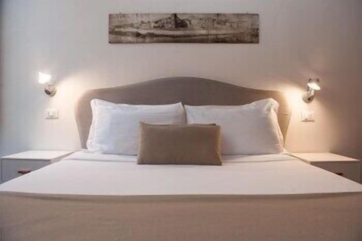 Una cama con sábanas blancas, una almohada marrón y dos lámparas de noche.