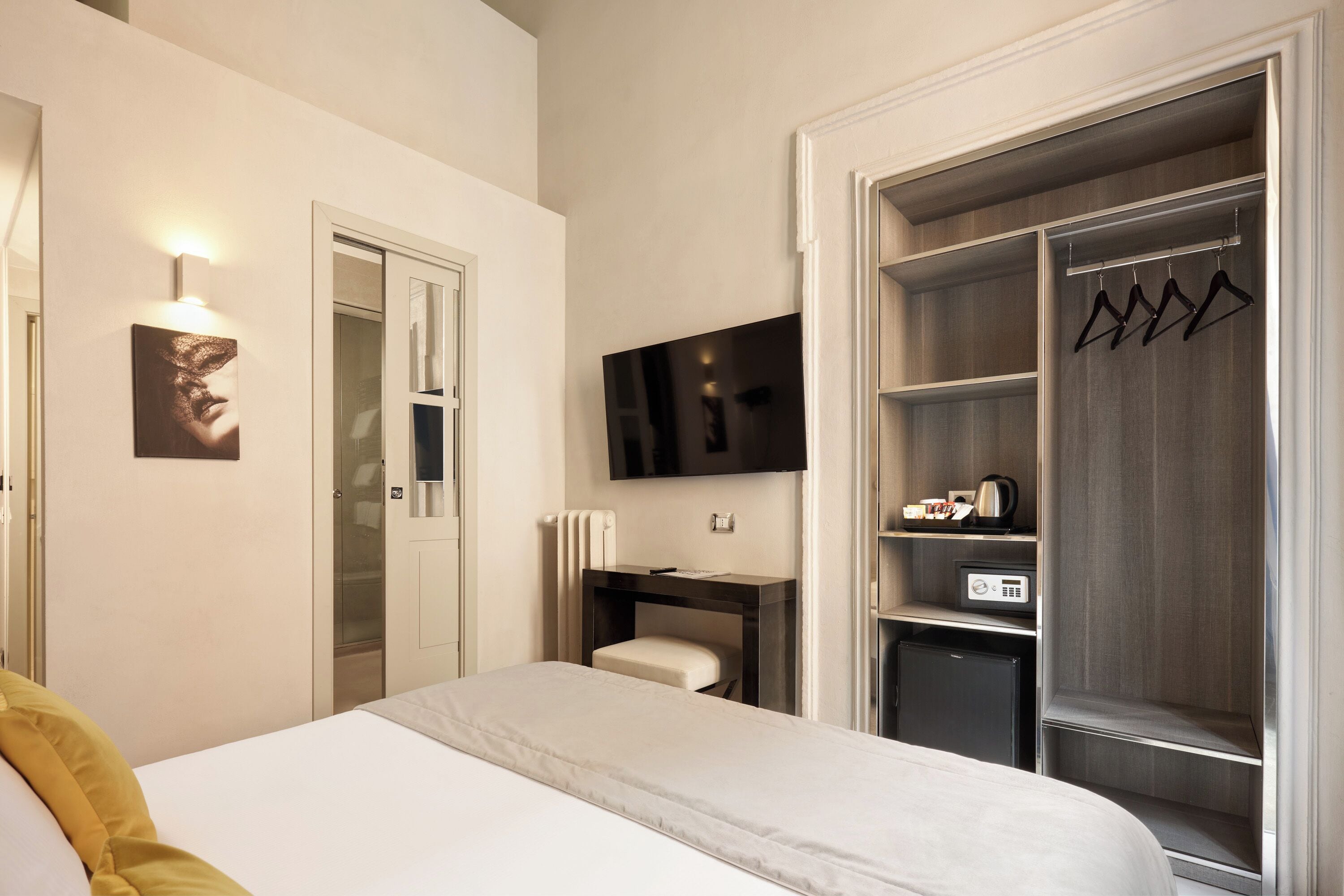 Habitación de hotel con cama, escritorio, televisor, armario y perchero.