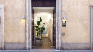 Entrada de un hotel con un arco central, una planta en maceta y un cartel que indica la ubicación.