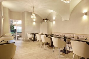 Un comedor moderno con sillas y mesas blancas, una araña y un espejo grande en la pared.