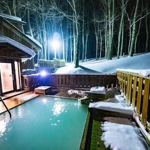 A heated outdoor pool surrounded by snow-covered wooden structures, with a forest in the background. - Kyukamura Nyuto-Onsenkyo (Senboku)