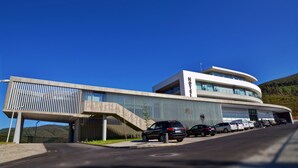 A modern hotel with a curved facade, a covered parking area, and a mountainous backdrop.