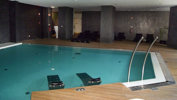 An indoor swimming pool with lounge chairs and a wooden deck.