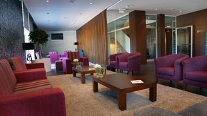 A modern lobby with red and purple upholstered seating, a wooden coffee table, and a stone wall.