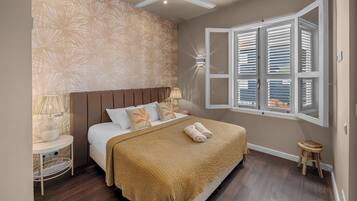 A bedroom with a bed, a nightstand, a lamp, a window with blinds, and a ceiling fan.