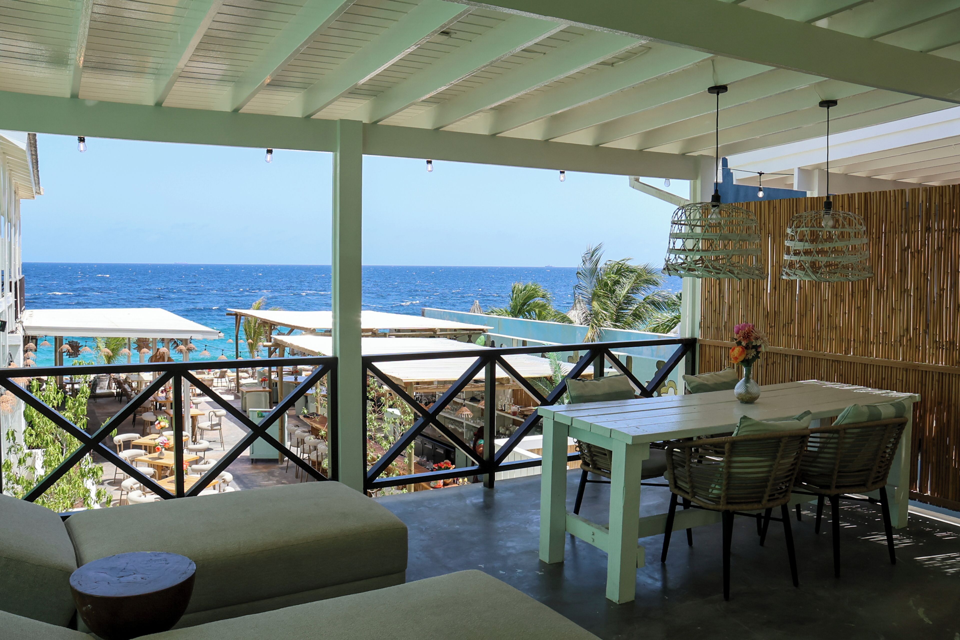 A covered outdoor area with a table and chairs, a view of the ocean, and a pool area.