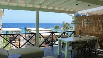 A covered outdoor area with a table and chairs, a view of the ocean, and a pool area.