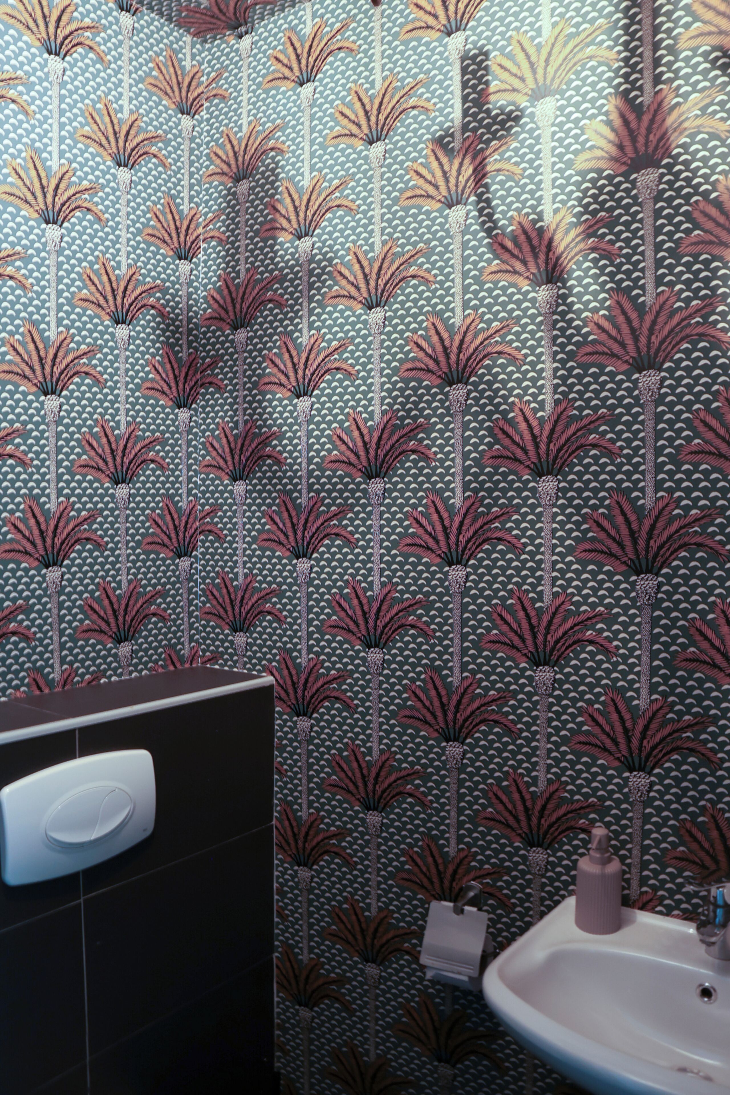 Un baño con papel tapiz estampado, un lavamanos blanco y un dispensador de jabón.