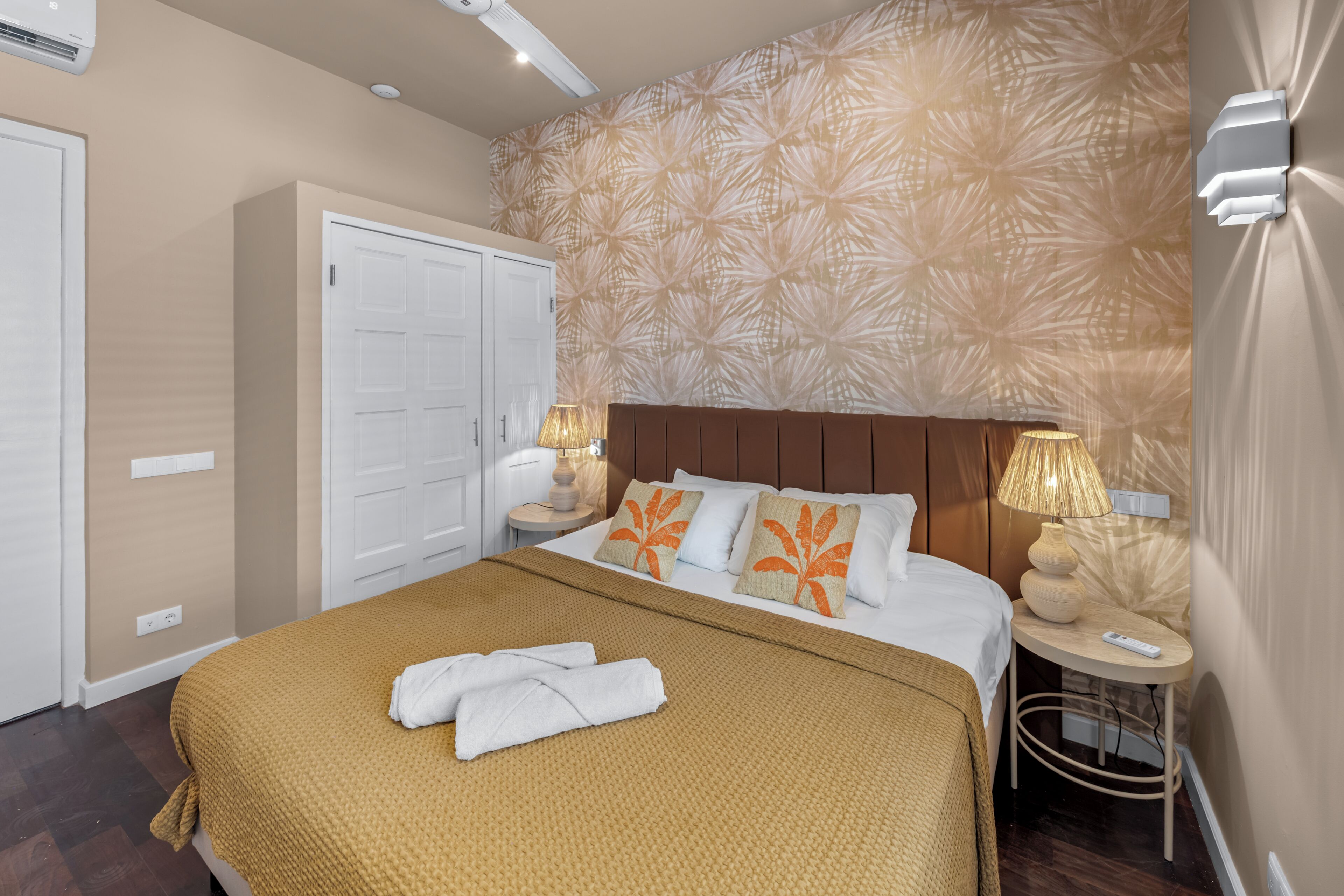 Ein Hotelzimmer mit Bett, Schrank, Nachttisch mit Lampe und Wand mit Blättermuster.