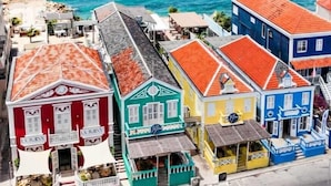 A coastal town with colorful buildings, a clear view of the ocean, and a street leading to a beach. - BijBlauw Hotel (Willemstad)