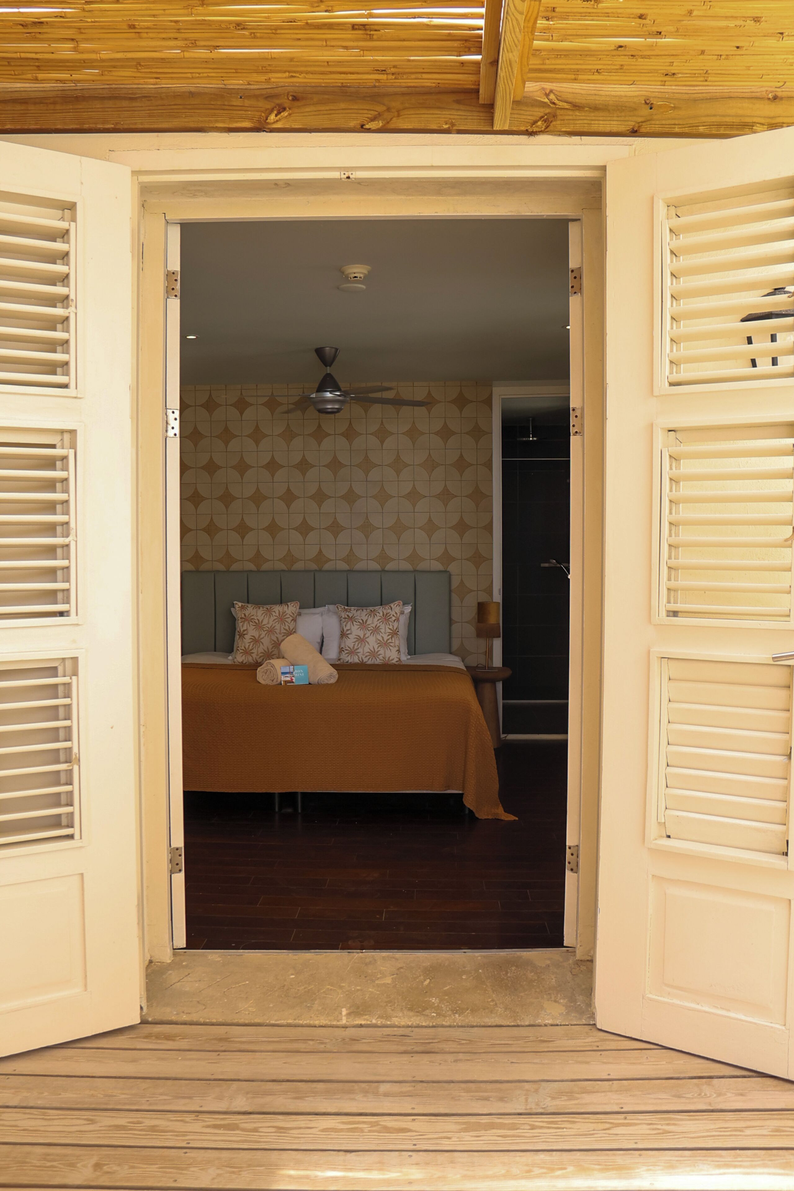 Puerta abierta a un dormitorio con una cama, cabecera y mesita de noche.