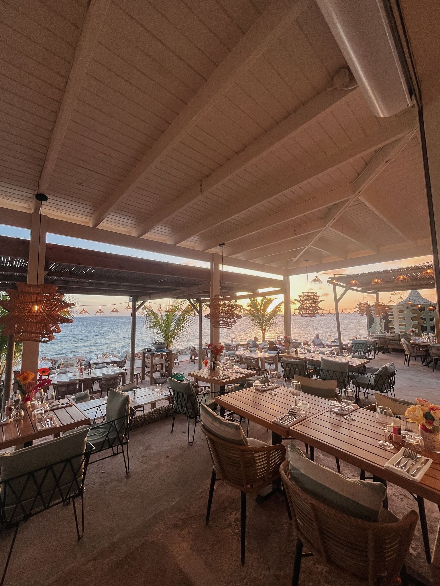 Un espace extérieur aménagé pour les repas, avec des tables et des chaises, donnant sur une plage.