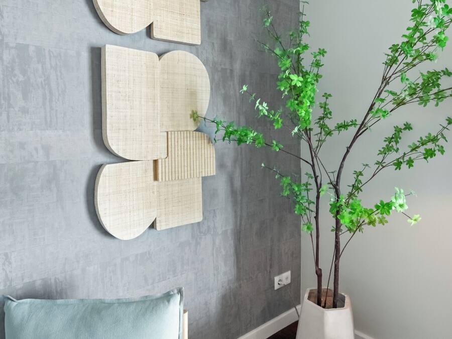 Een moderne woonkamer met een grijze, gestructureerde muur, een lichtblauwe bank, een houten bijzettafeltje en een pot met groene bladeren.