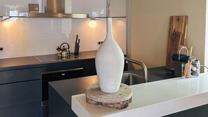 A modern kitchen with a central island, a white vase with branches, and a wooden cutting board. - BijBlauw Hotel (Willemstad)