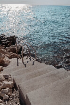A concrete staircase leading to a rocky shoreline with a metal handrail. - BijBlauw Hotel (Willemstad)