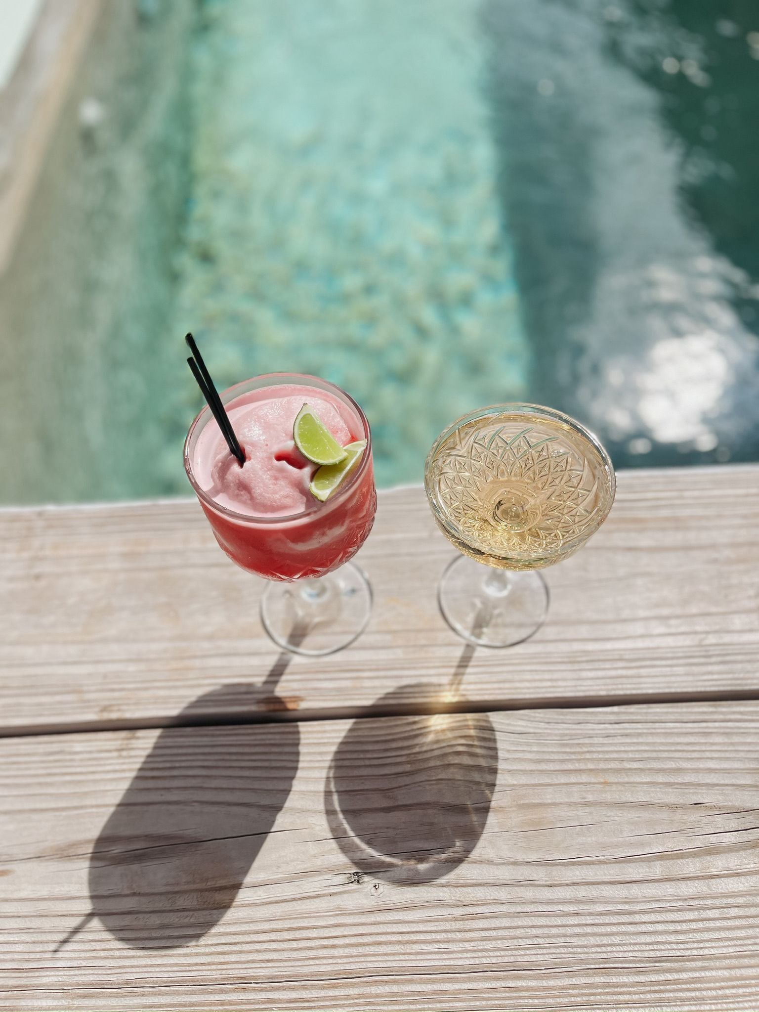 Deux boissons sur une terrasse en bois, près d’une piscine.