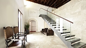 A modern interior with a marble floor, a staircase with glass railings, and antique-style furniture.