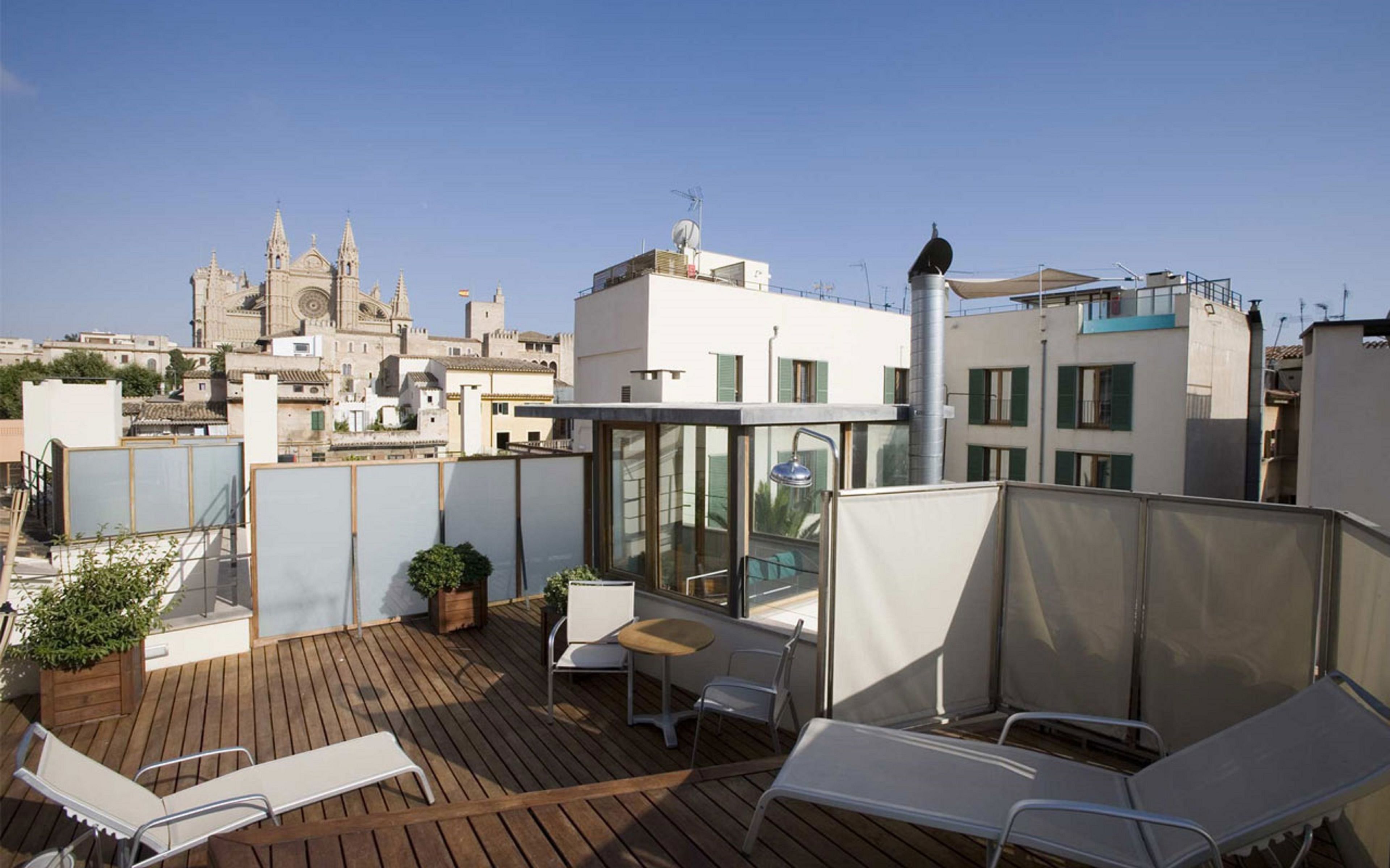 Una terraza en la azotea con suelo de madera, sillones blancos, una mesita y plantas en macetas.