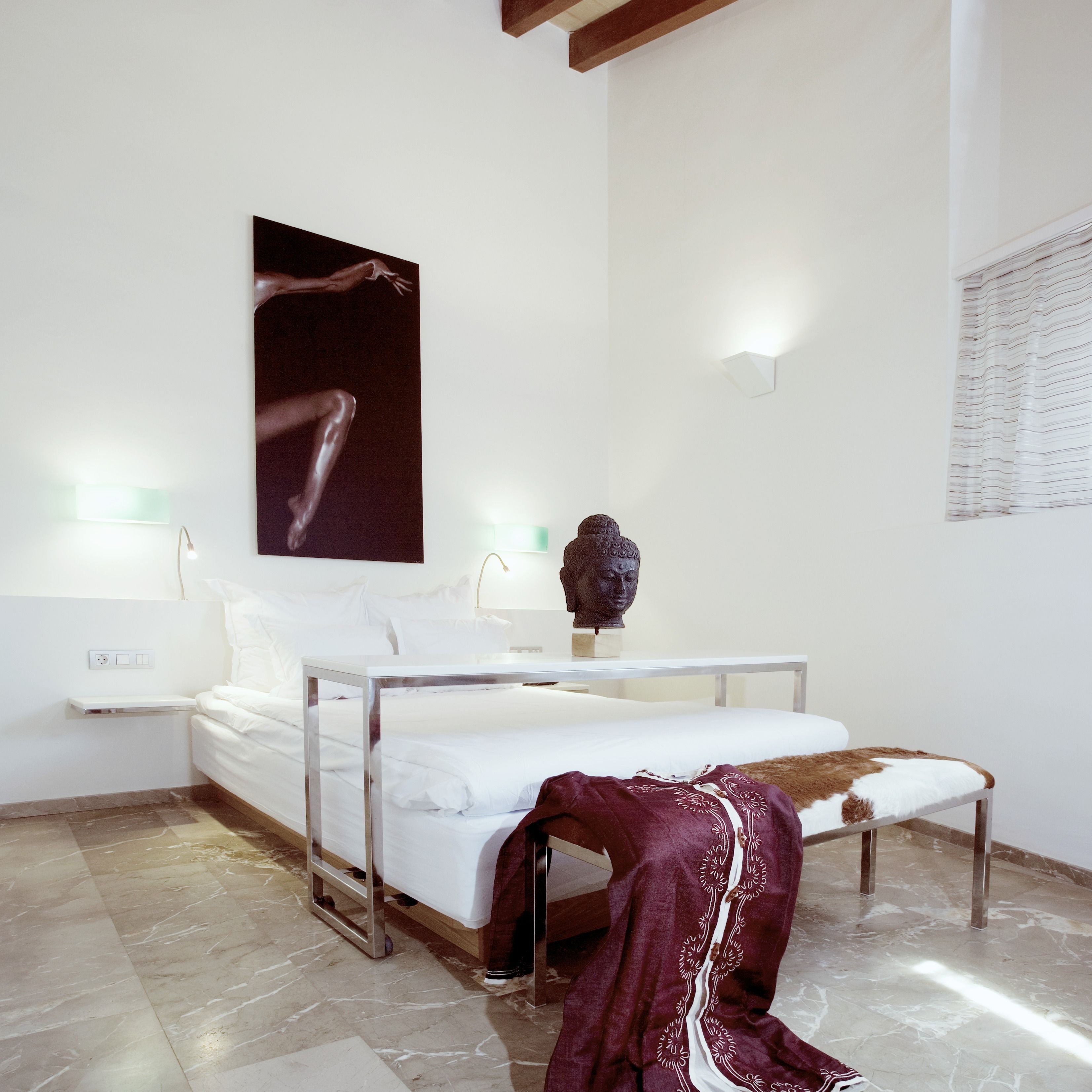 A hotel room with a bed, bedside lamps, a headboard, a nightstand, a statue, and a wall-mounted artwork.