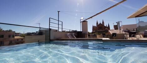 Una piscina en la azotea con agua cristalina, vista de un edificio histórico y cielo soleado.