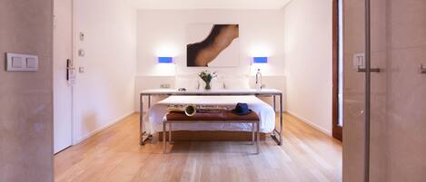Una habitación de hotel moderna con una cama grande, lámparas de noche, una mesita de noche y una obra de arte colgada en la pared.