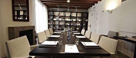 A conference room with a long table, chairs, a bookshelf, and a fireplace.
