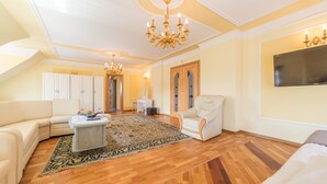 A spacious living room with a large chandelier, a sofa, a chair, and a television on the wall. - Motelik Mister (Mielno)