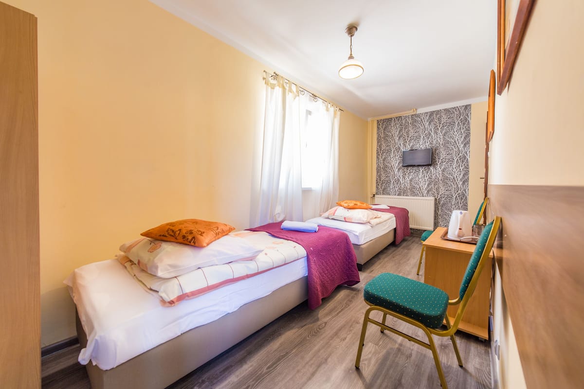Habitación de hotel con dos camas, un escritorio, una silla, un televisor y un papel tapiz estampado.