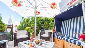 An outdoor seating area with wicker furniture, a white table with food, and a striped blue and white canopy. - Motelik Mister (Mielno)