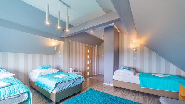 A bedroom with two beds, a blue rug, and a sloped ceiling with recessed lighting. - Motelik Mister (Mielno)