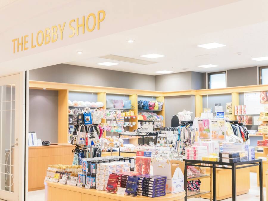 A store named "THE LOBBY SHOP" with shelves of bags, accessories, and food items.