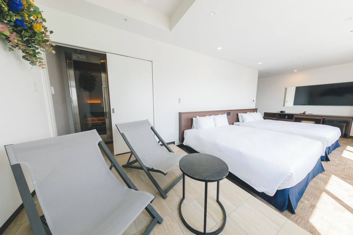 A hotel room with two beds, a TV, a desk, and a seating area with chairs and a small table.