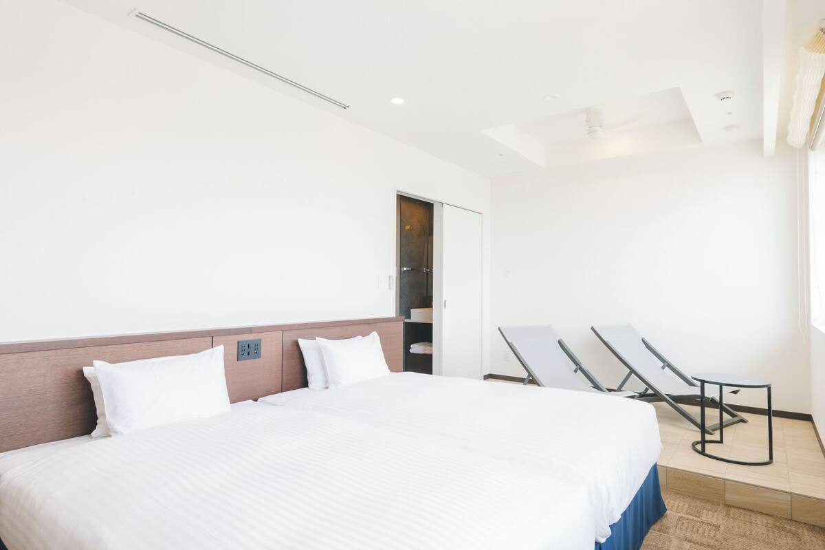 A hotel room with a large bed, a wardrobe, a mirror, and a sun lounger.