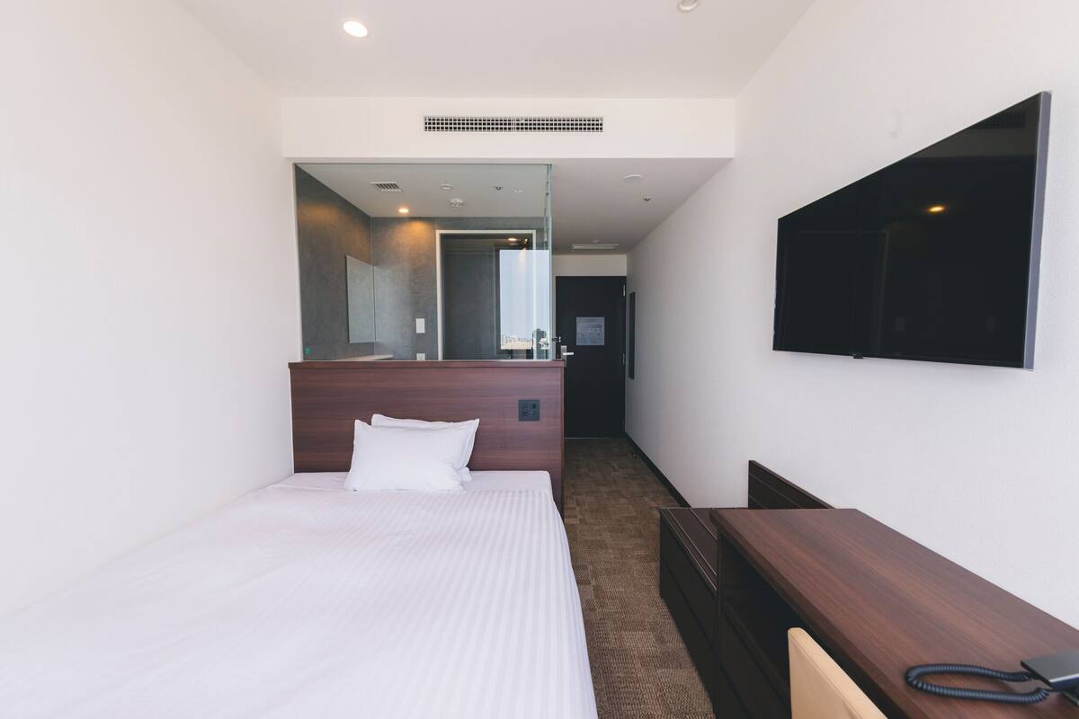 A hotel room with a bed, a desk, a mirror, and a TV.