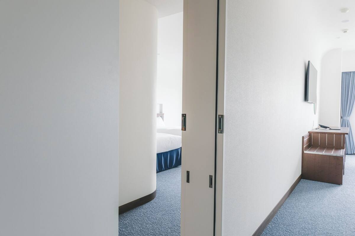 A hotel room with a bed, a desk, a mirror, and a door.