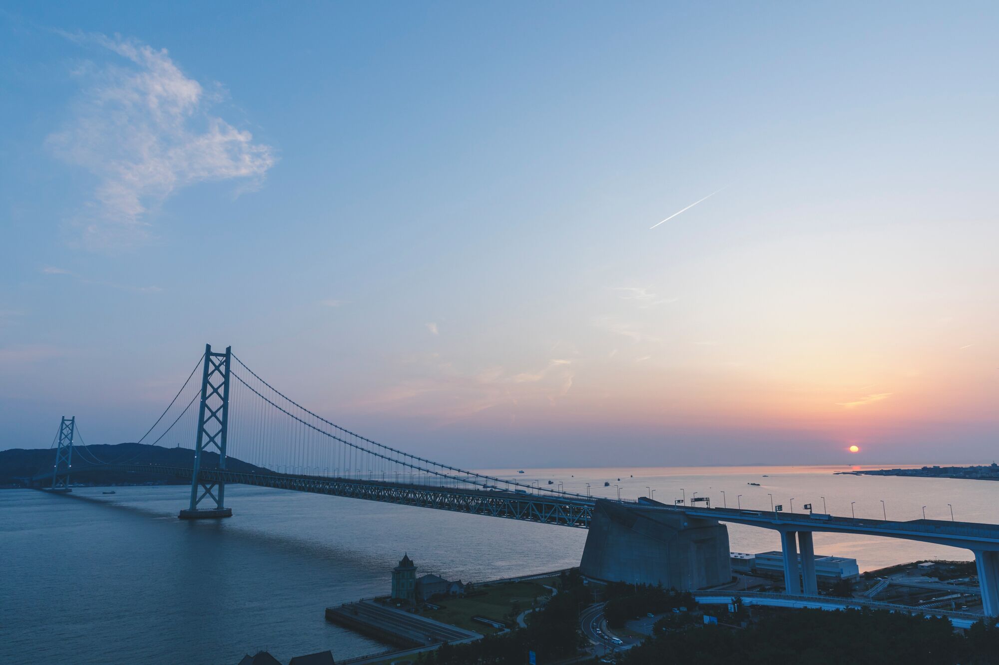 Un puente colgante imponente que cruza una masa de agua, con un atardecer de fondo.