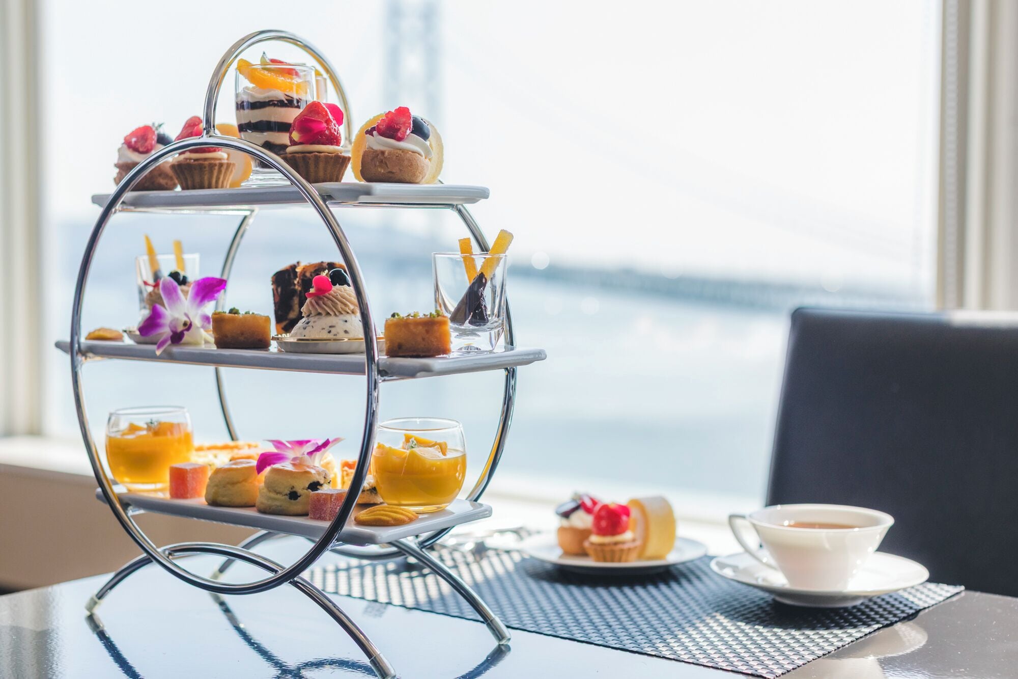 A three-tiered dessert stand with various pastries and a cup of coffee on a table with a view.