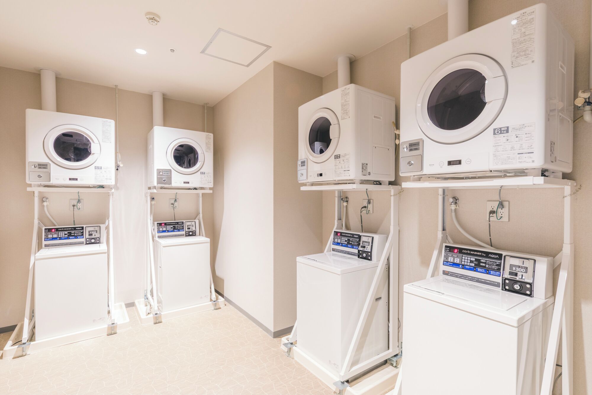 A laundry facility with multiple washing machines and dryers, each with control panels and hoses.