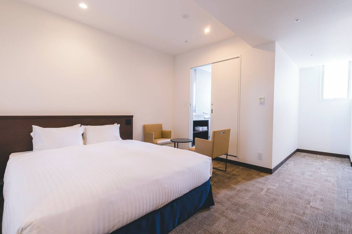 A hotel room with a large bed, a small table, two chairs, and a mirror.