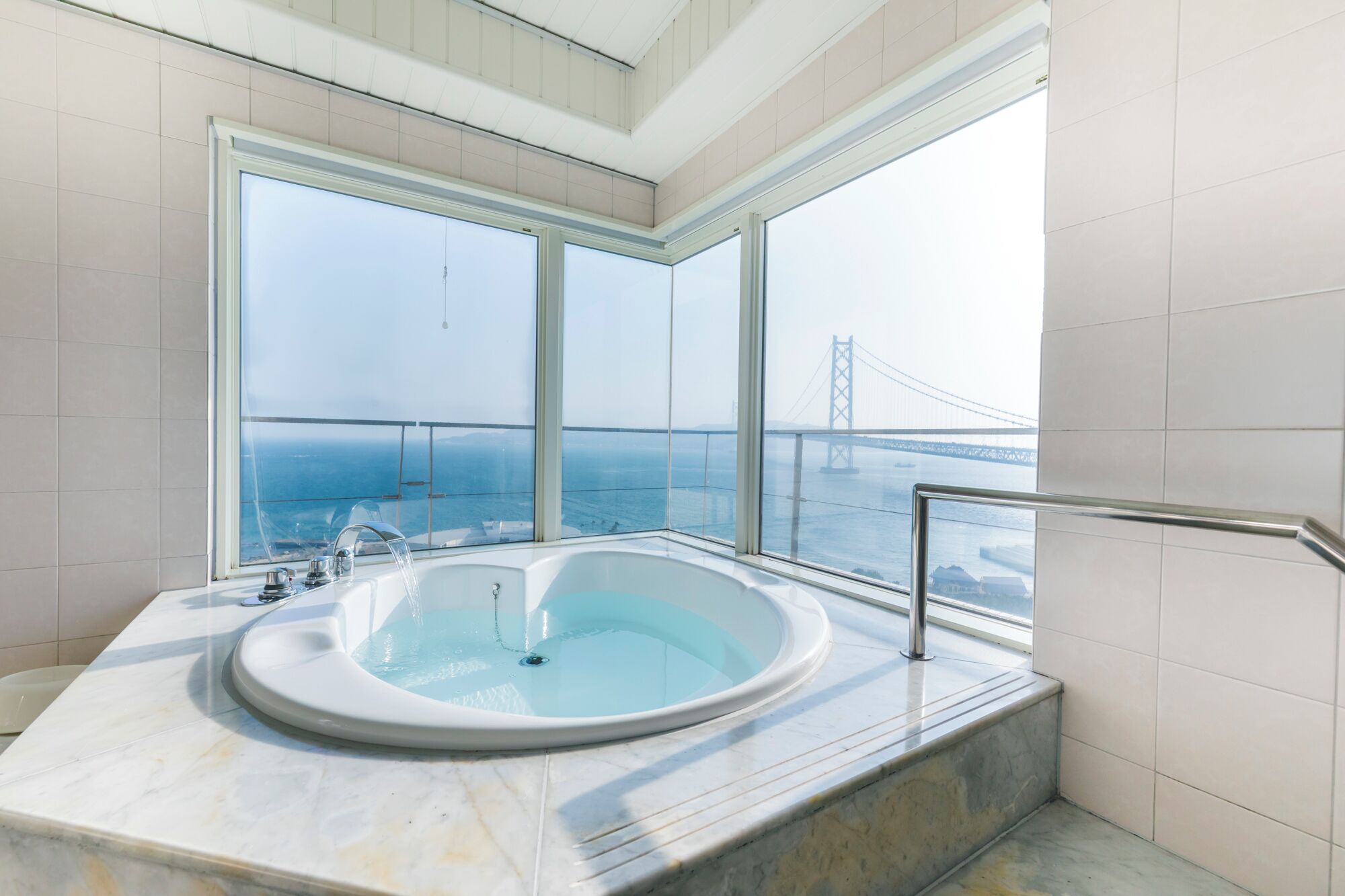 A modern bathroom with a large bathtub, a view of a bridge, and a balcony.