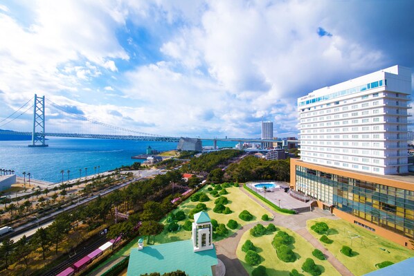 A modern hotel with a large glass facade, a central courtyard with greenery, and a view of a bridge and water body. - Seaside Hotel Maiko Villa Kobe (Kobe)
