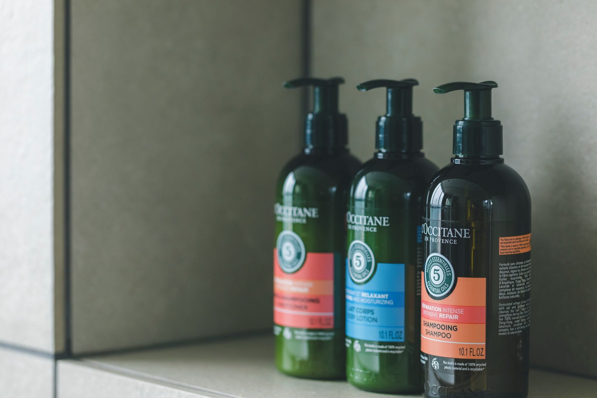 Three bottles of Occitané shampoo on a shelf.