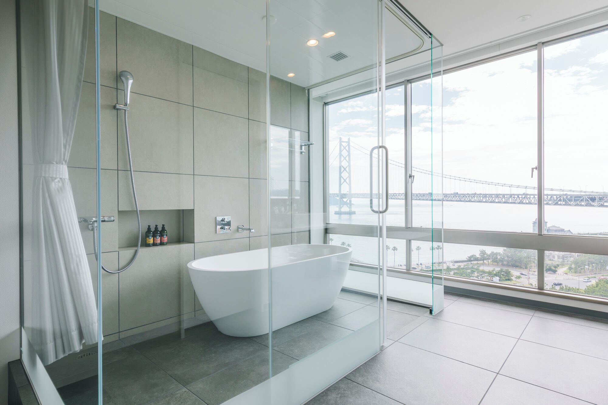 Ein modernes Badezimmer mit freistehender Badewanne, einer Glasdusche und Blick auf eine Brücke durch große Fenster.