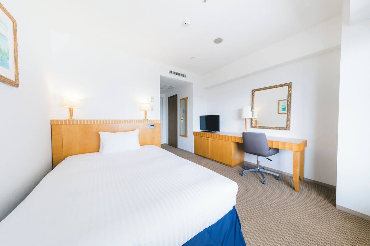 A hotel room with a large bed, a desk with a chair, a television, and a mirror.