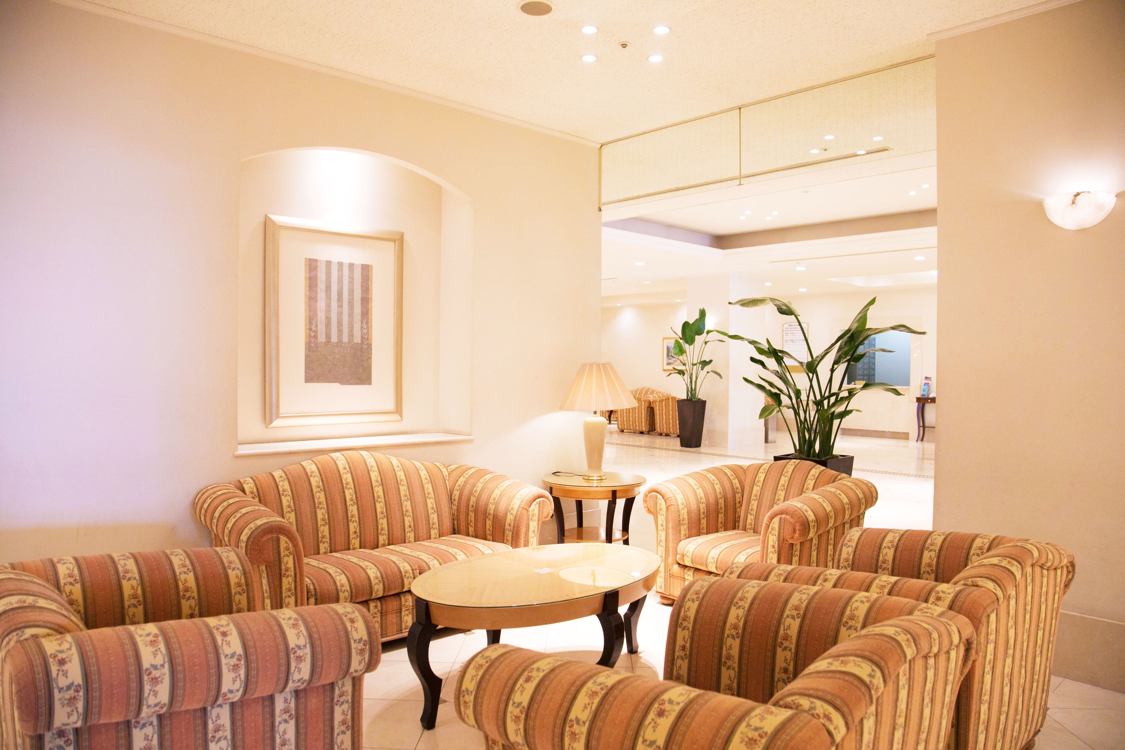 A hotel lobby with striped armchairs, a round table, and a potted plant.