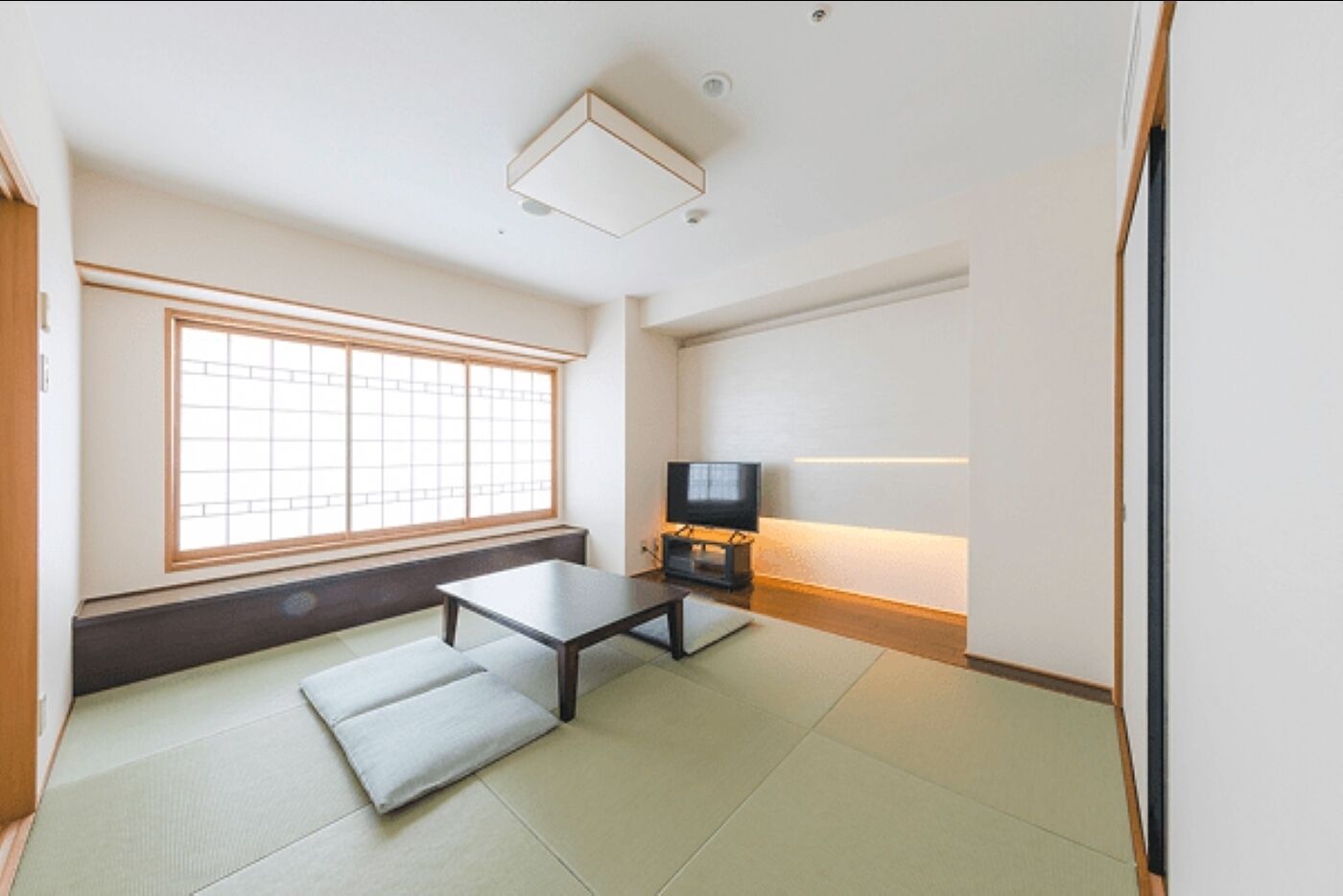 Una habitación con esteras de tatami, una mesa baja, un televisor y un ventanal con un diseño de cuadrícula.