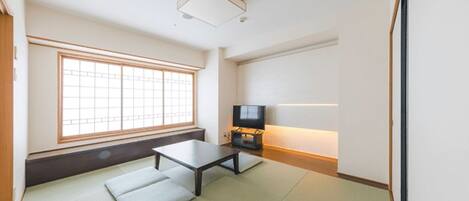 Una habitación con esteras de tatami, una mesa baja, un televisor y un ventanal con un diseño de cuadrícula.