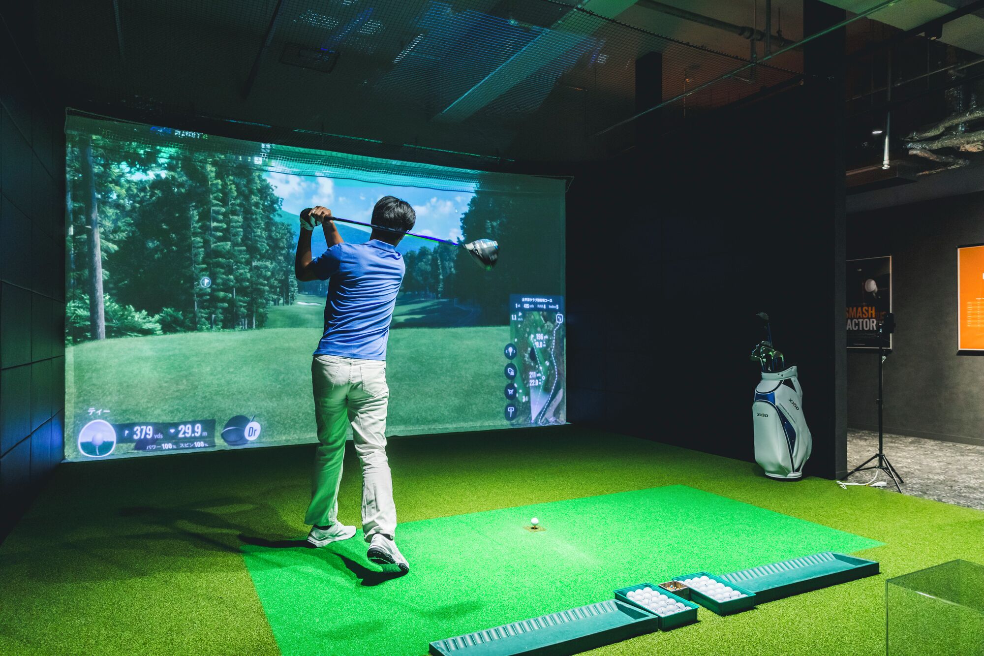 A person playing golf indoors with a large screen displaying a golf course.