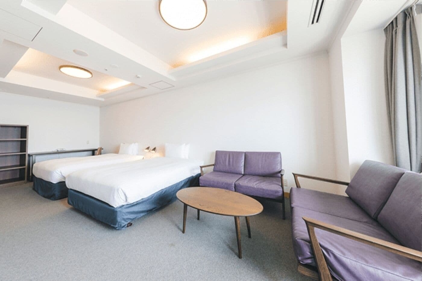 A hotel room with a bed, two sofas, a small table, and a ceiling light.