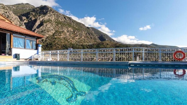 Una piscina con agua azul cristalina, un edificio con techo rojo y un paisaje montañoso de fondo.